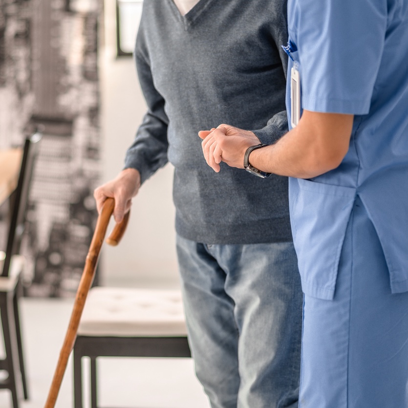 Medical worker helping his patient to walk with a cane